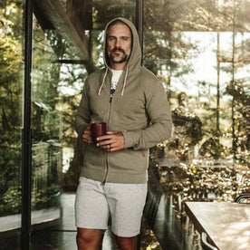 our fit model wearing The Après Hoodie in Olive—holding coffee, walking toward camera