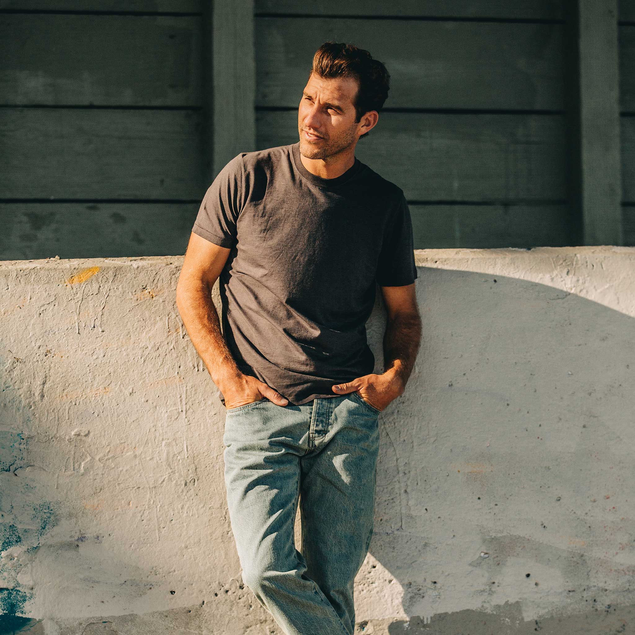 our fit model wearing The Standard Issue Tee in Charcoal Hemp—leaning against wall, Knits by Taylor Stitch