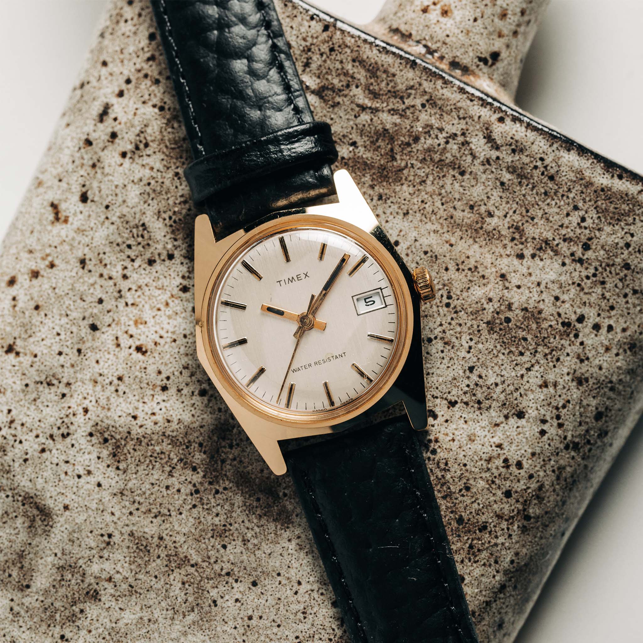 flatlay of the 1978 Timex Gold Marlin on a ceramic background, Accessories by Taylor Stitch