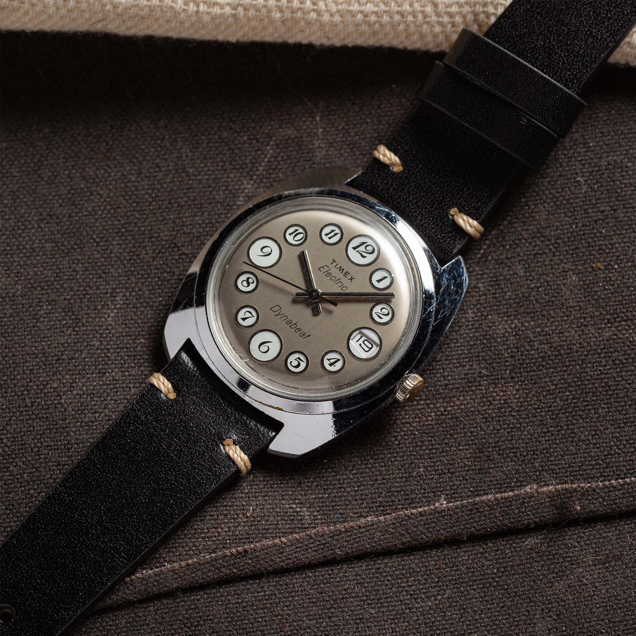 flatlay of 1975 Timex Electric Dynabeat "Rotary" against against a brown background, Accessories by Taylor Stitch