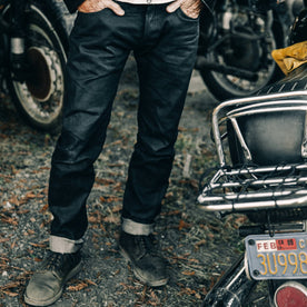 fit model wearing The Democratic Jean in Black Over-dye Selvage, standing near bike