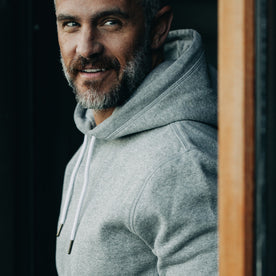 our fit model wearing The Heavy Bag Hoodie in Heather Grey Fleece closeup while looking over left shoulder smirking