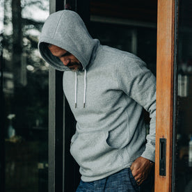 our fit model wearing The Heavy Bag Hoodie in Heather Grey Fleece with the hood up and looking down