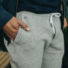 our fit model wearing The Heavy Bag Pant in Heather Grey Fleece closeup with right hand in pocket showing TS embroidered logo