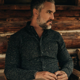 our fit model wearing The Jack in Coal Donegal—sitting, looking right next to cabin
