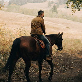 fit model wearing The Lined Long Haul Jacket in Harvest Tan Dry Wax, back on horse