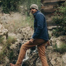 fit model wearing The Quilted Jacket in Indigo Boss Duck, standing on rocks