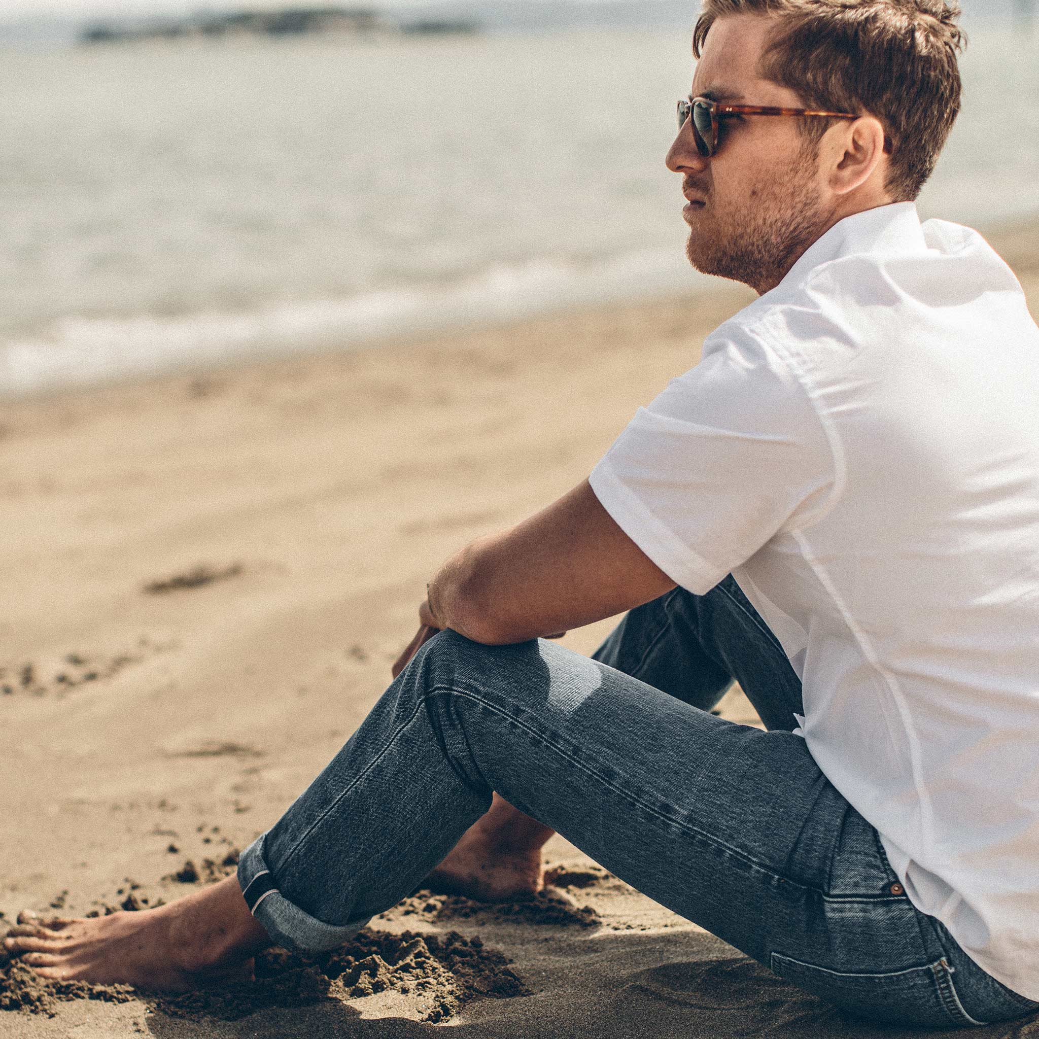 Garrett sitting on the beach in the 24 Month Wash Slim cut denim, Denim by Taylor Stitch