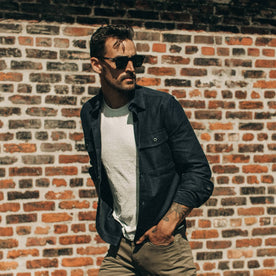 fit model wearing The Point Shirt in Navy Reverse Sateen, looking right, brick wall behind