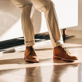 The Unlined Chukka in Butterscotch Weatherproof Suede—pants cuffed, sitting against couch