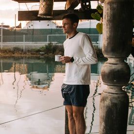 fit model wearing The Heavy Bag Long Sleeve in Natural, holding coffee near water