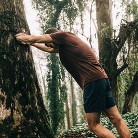 fit model wearing The Merino Tee in Wine, stretching against tree