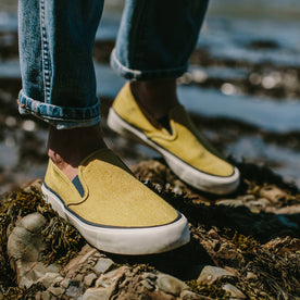 fit model wearing The Sano Slip-On in Gold Boss Duck, standing on rocks near the coast