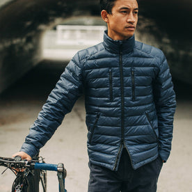 out fit model wearing The Taylor Stitch x Mission Workshop Farallon Jacket in Midnight Blue—standing with bike