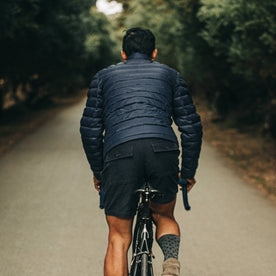 out fit model wearing The Taylor Stitch x Mission Workshop Farallon Jacket in Midnight Blue—back shot riding bike