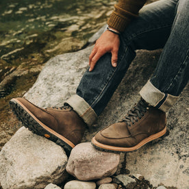 our fit model wearing The Scout Boot in Espresso Grizzly—sitting on rocks