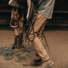 fit model wearing The Slim All Day Pant in Rustic Oak Organic Selvage, next to saddle